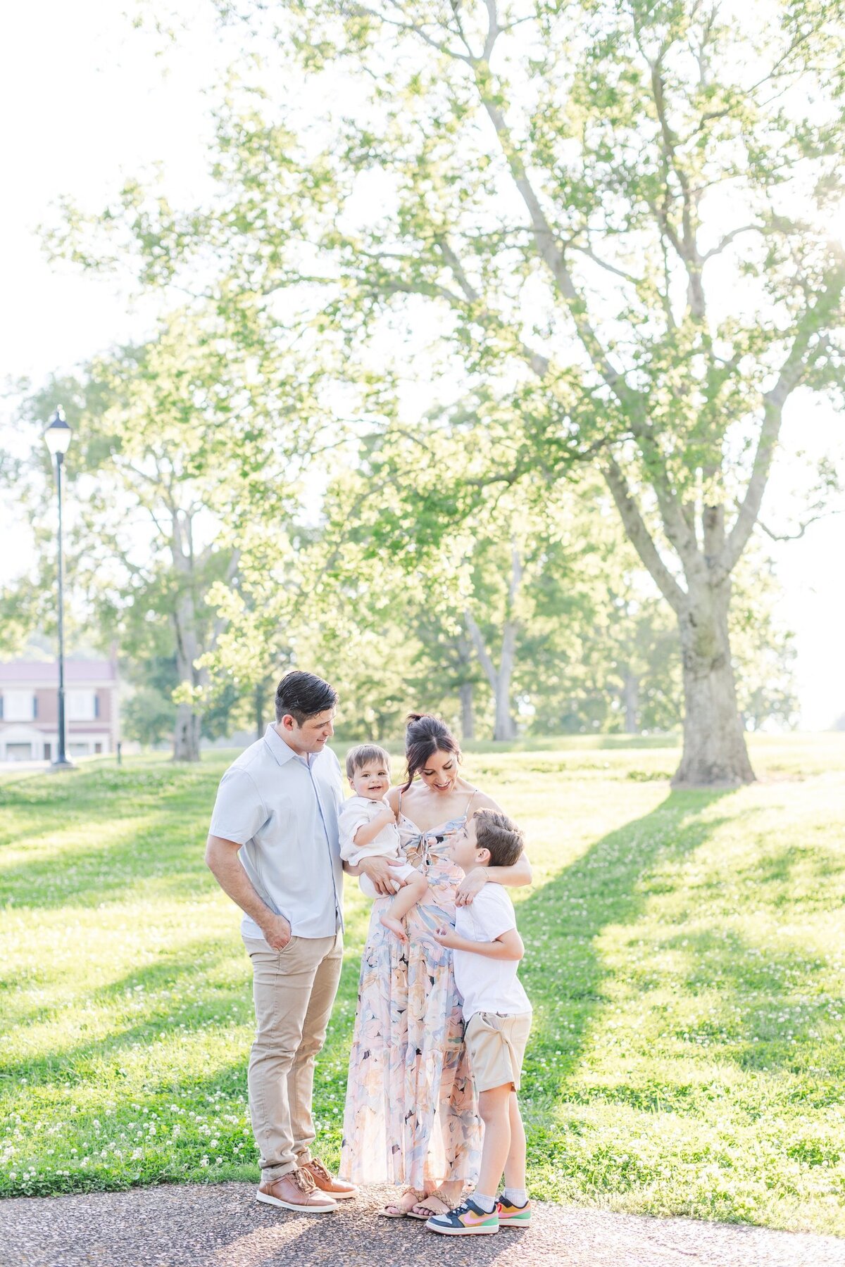 Family of four, wearing bright pastel colors all laugh together during spring in Brentwood, TN while baby boy smiles at camera