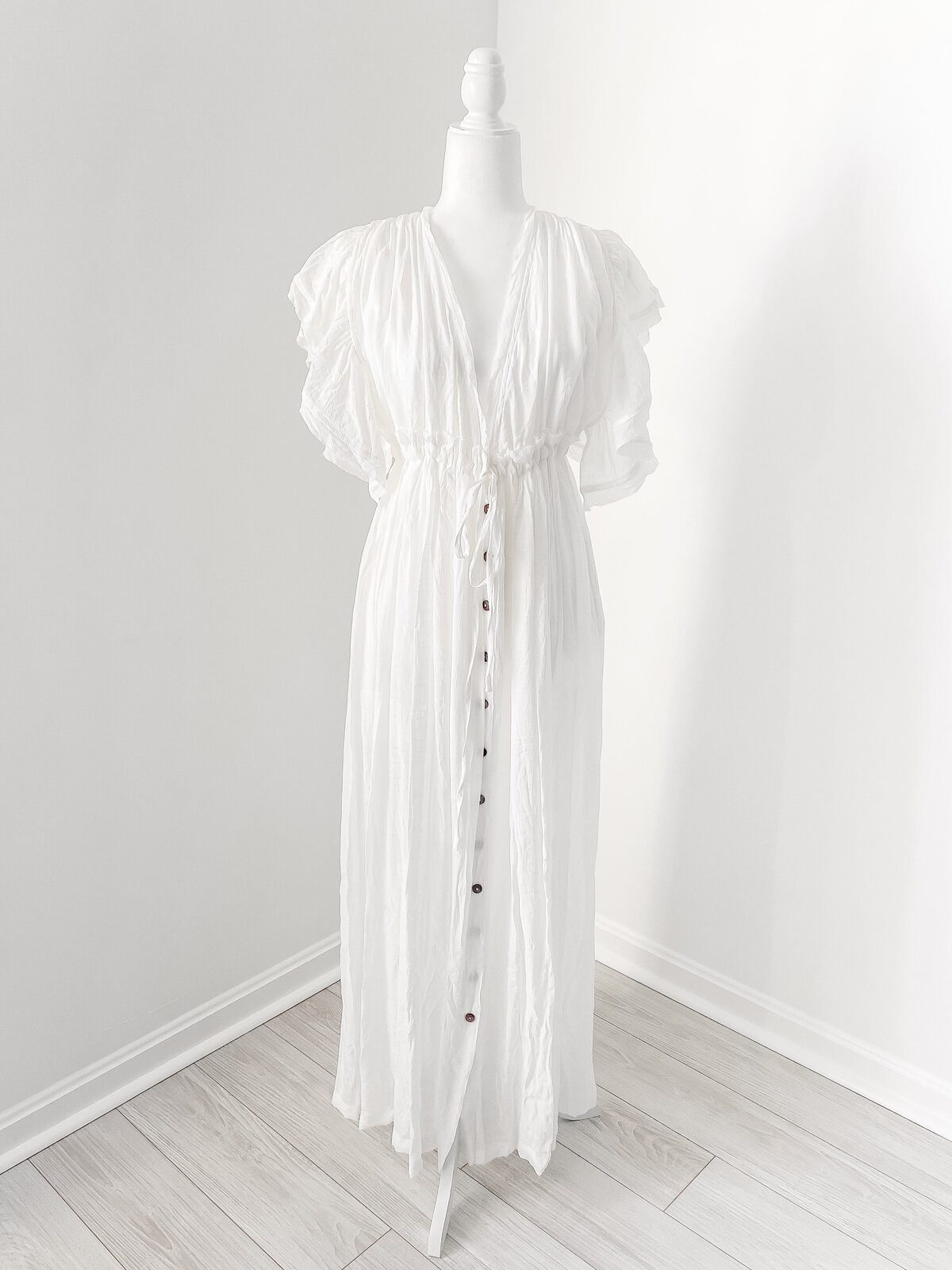 A DC Newborn Photographer photo of a long white dress with flutter sleeves and brown buttons down the front and a deep v neck