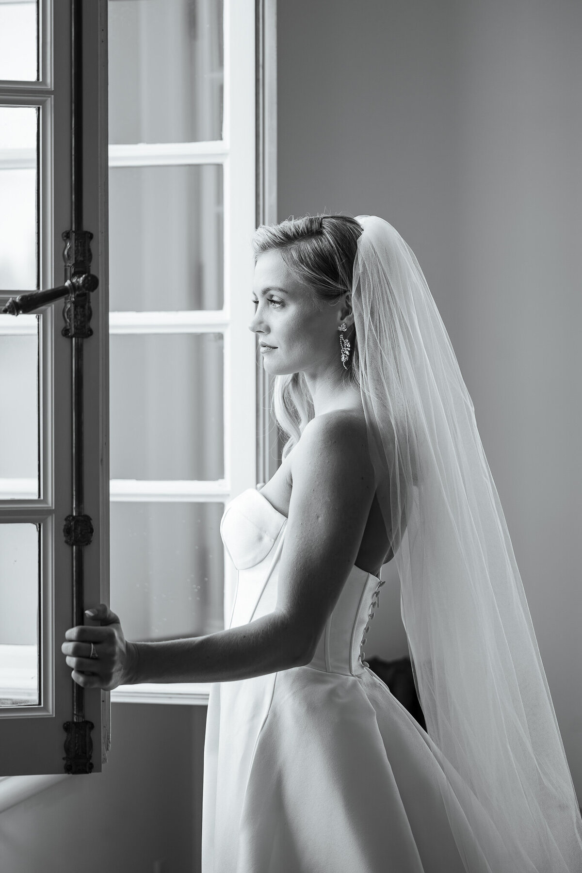 A blonde bride at a window in her bridal suite enjoying her Wilmington wedding photos