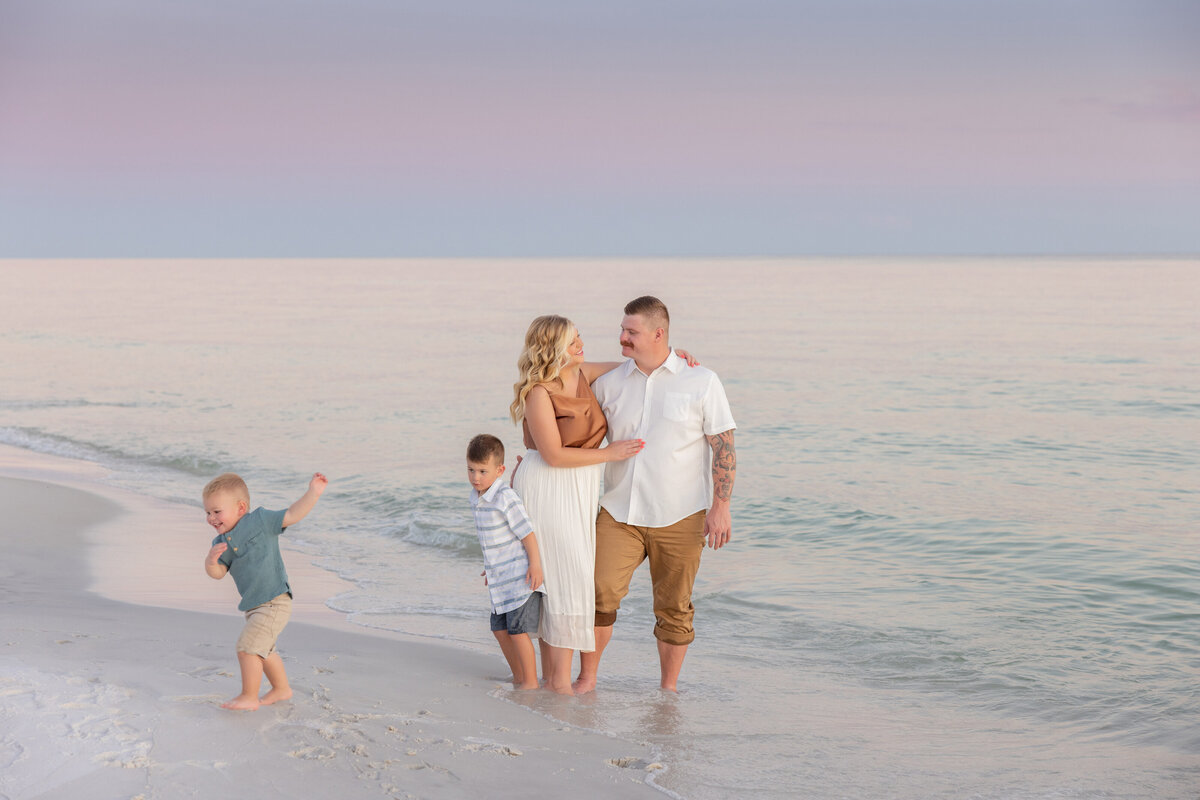 Two kids playing in the waves as their parents stand next to them