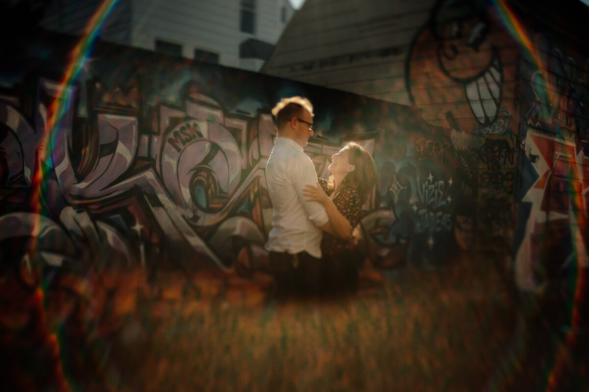 San Francisco urban couples photography session with graffiti in backdrop and circle of rainbow lens flare