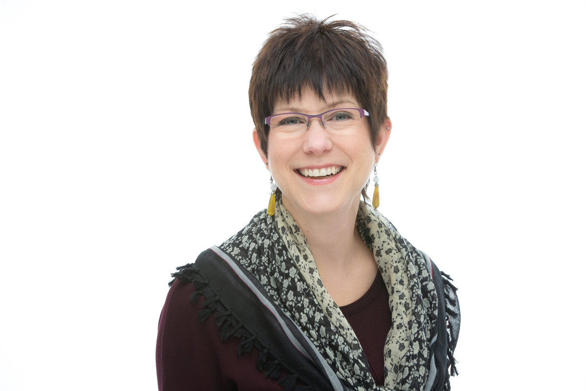 A businesswoman with short dark hair and glasses poses for a professional corporate headshot photo on a high key white background at Janel Lee Photography studios in Cincinnati Ohio
