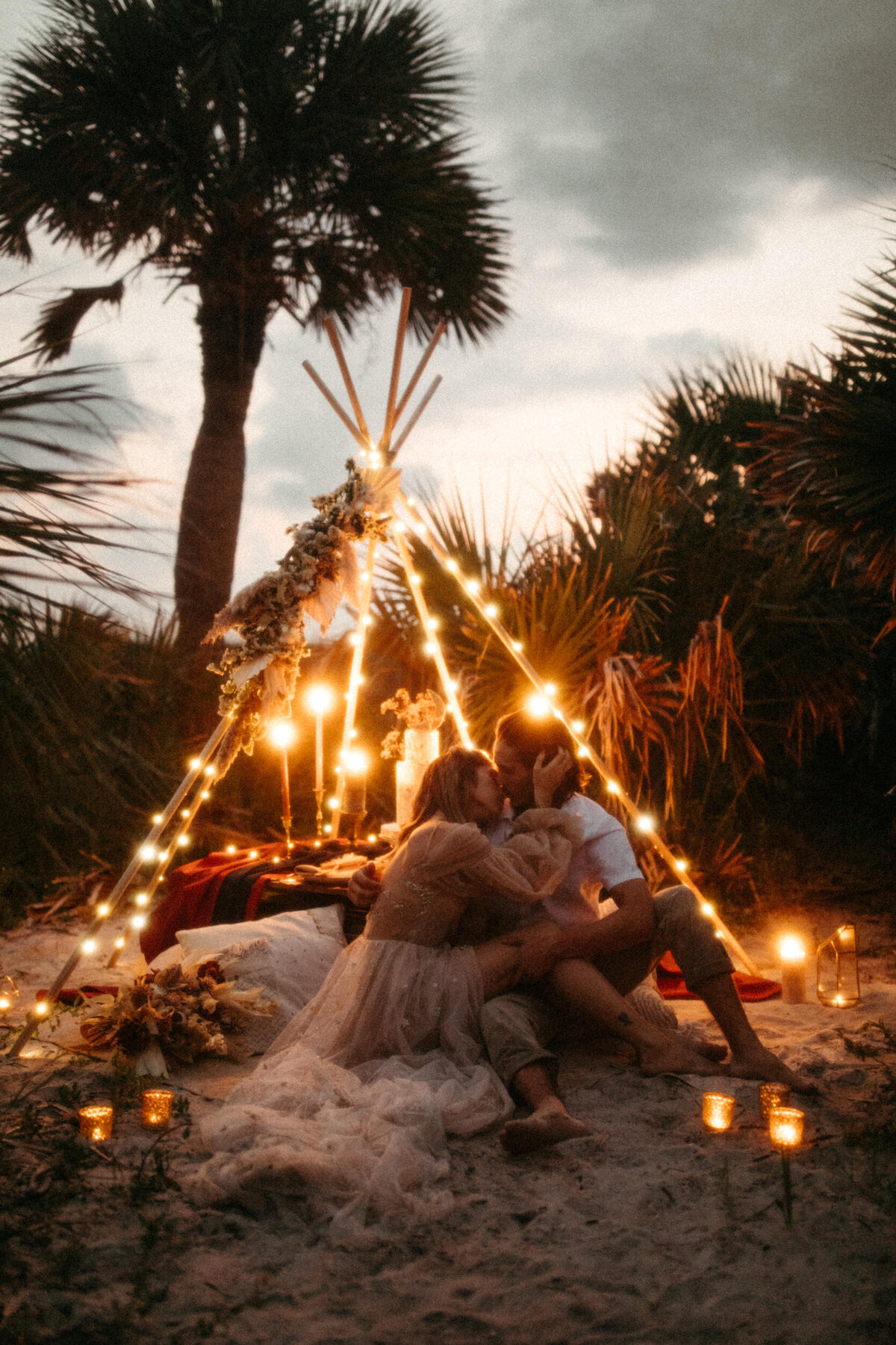 Couple kissing and sitting on the ground at their intimate candlelit beach elopement reception setup