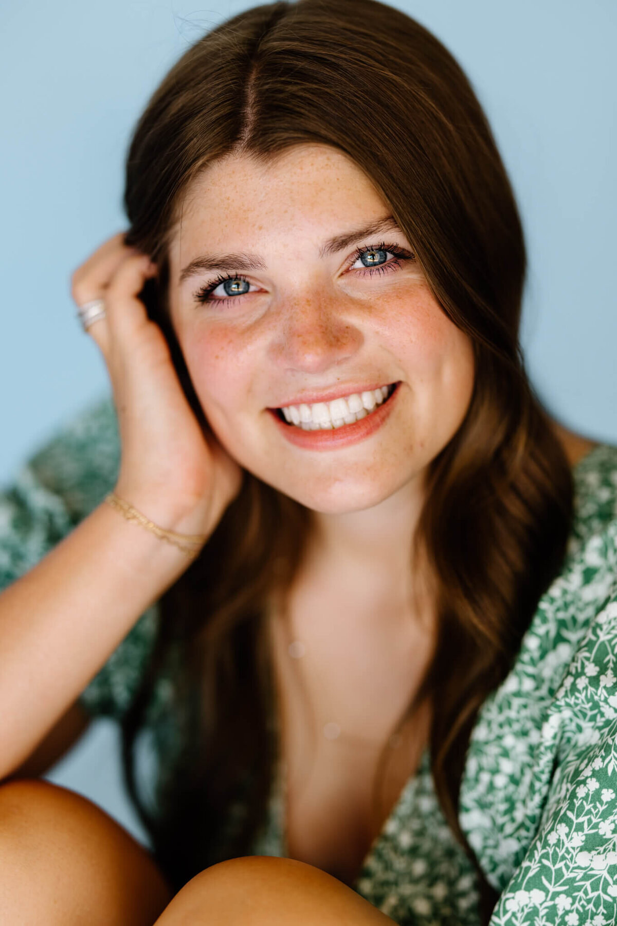 headshot portraits of Marshall Texas 2023 graduate in green floral blouse, white shorts, and light blue background