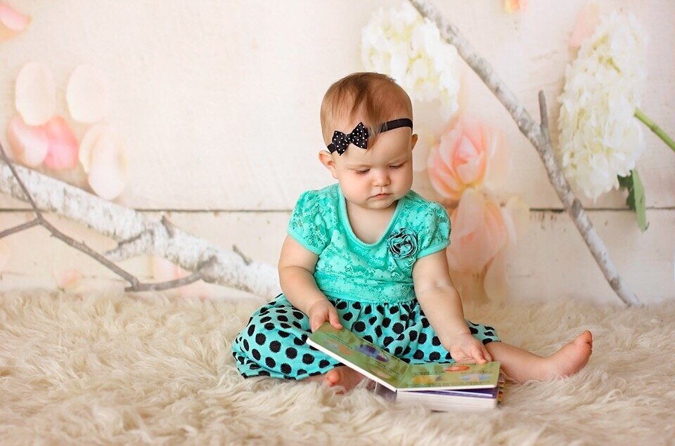 My daughter at a year old reading a book in a studio photography setting.