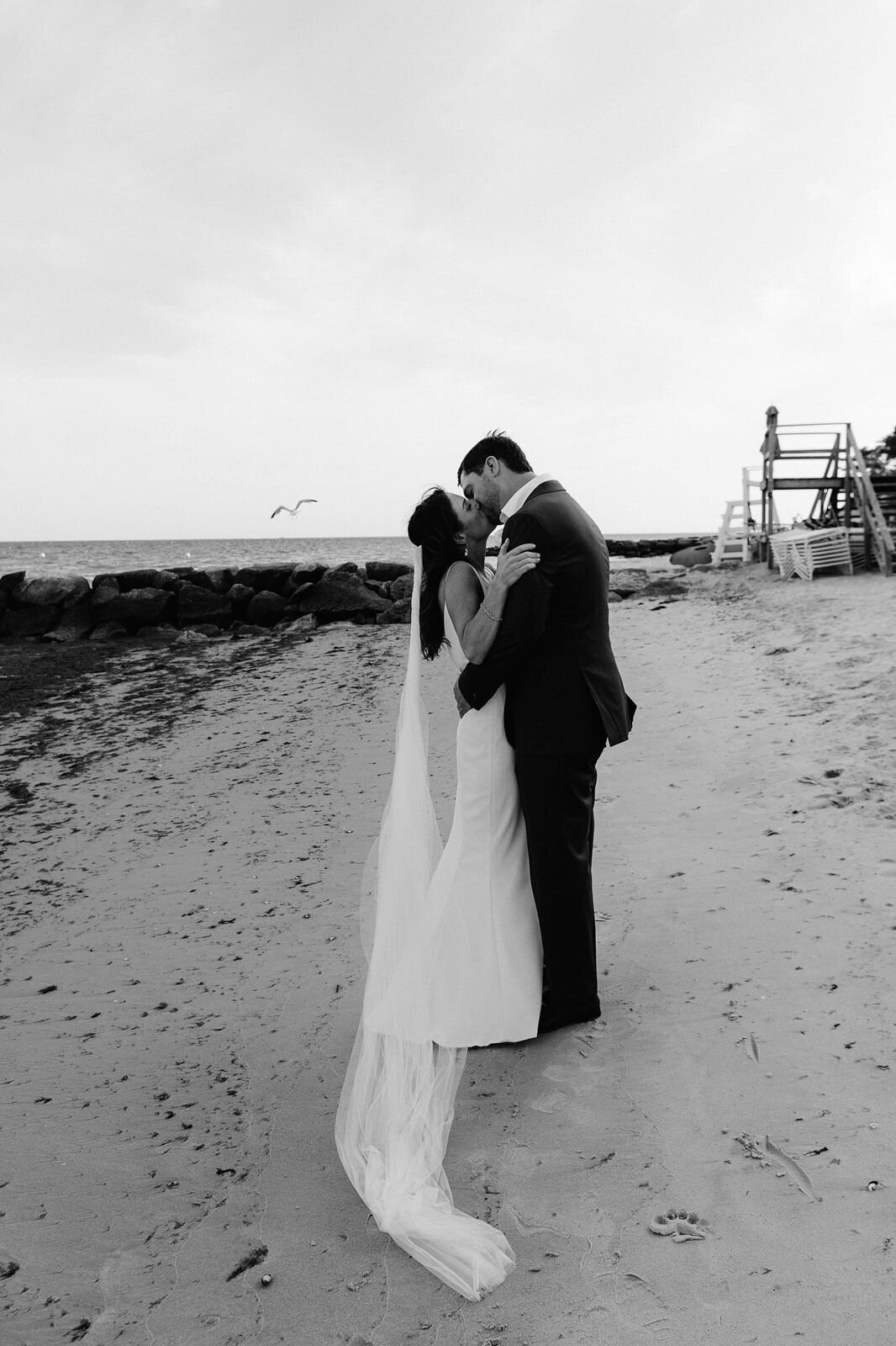 Black and white photo of the bride and the groom kissing each other on a seashore in Cape Cod, MA.