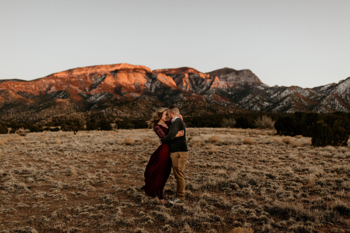 Engaged couple walking in the Albuquerque desert with the mountain behind them