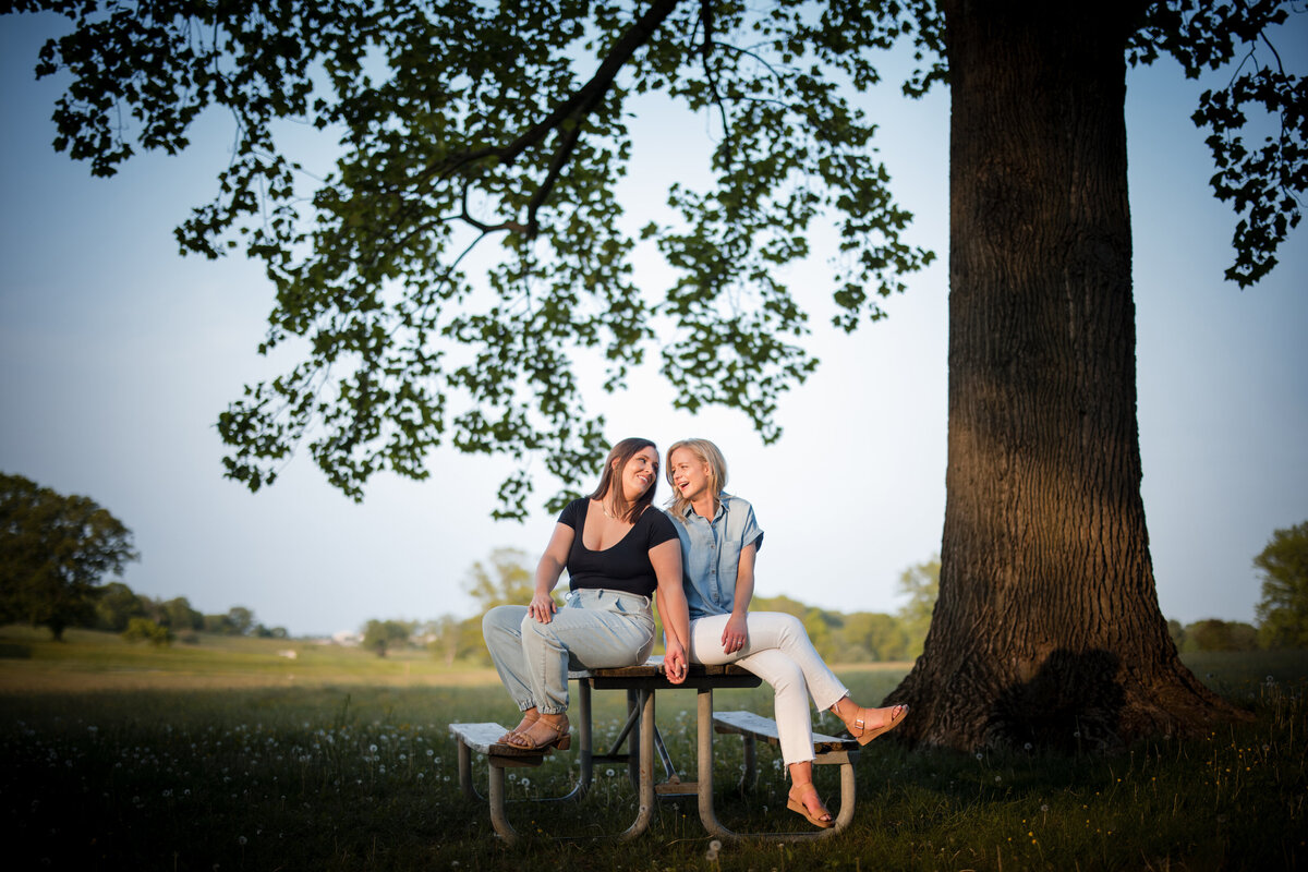 Two women sitting on a picnic table holding hands and smiling.