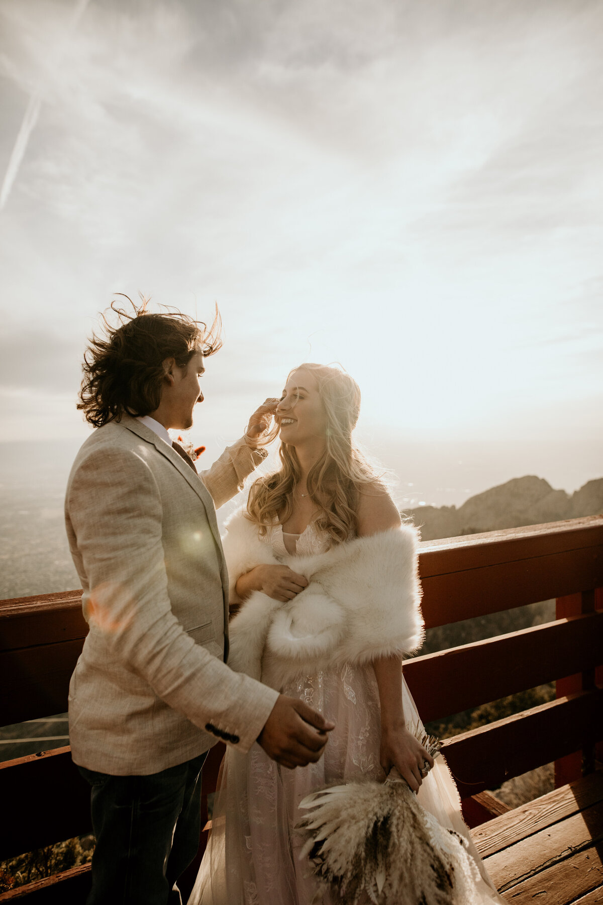 bride and groom together with hair flying around in wind on top of Sandia Mountains