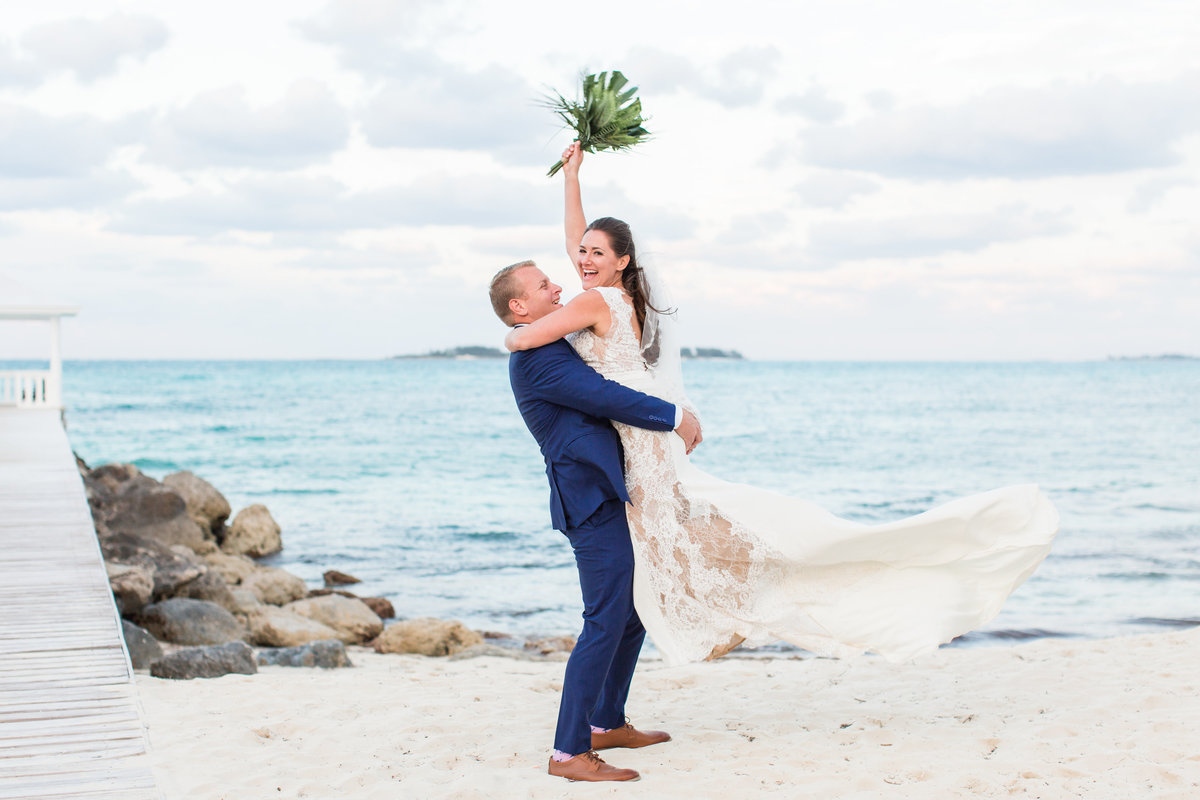 Groom holding bride in the air on the beach in the Bahamas