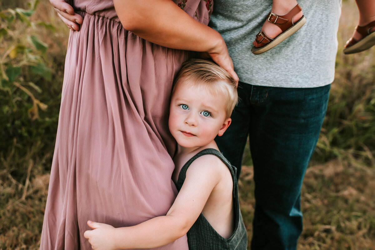 Little boy hugging mom's dress and looking at the camera.