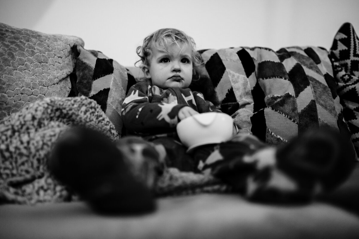 Little girl sat with a bowl of cereal on sofa duuring family photoshoot