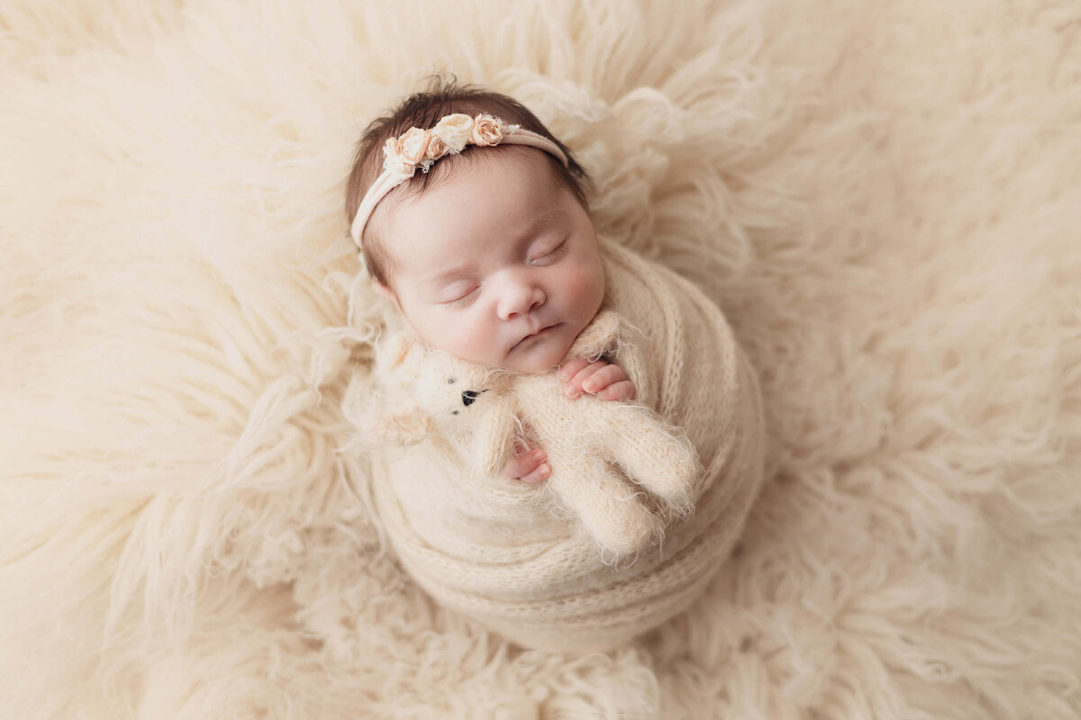 baby girl sleeping hugging teddy bear in cream blanket