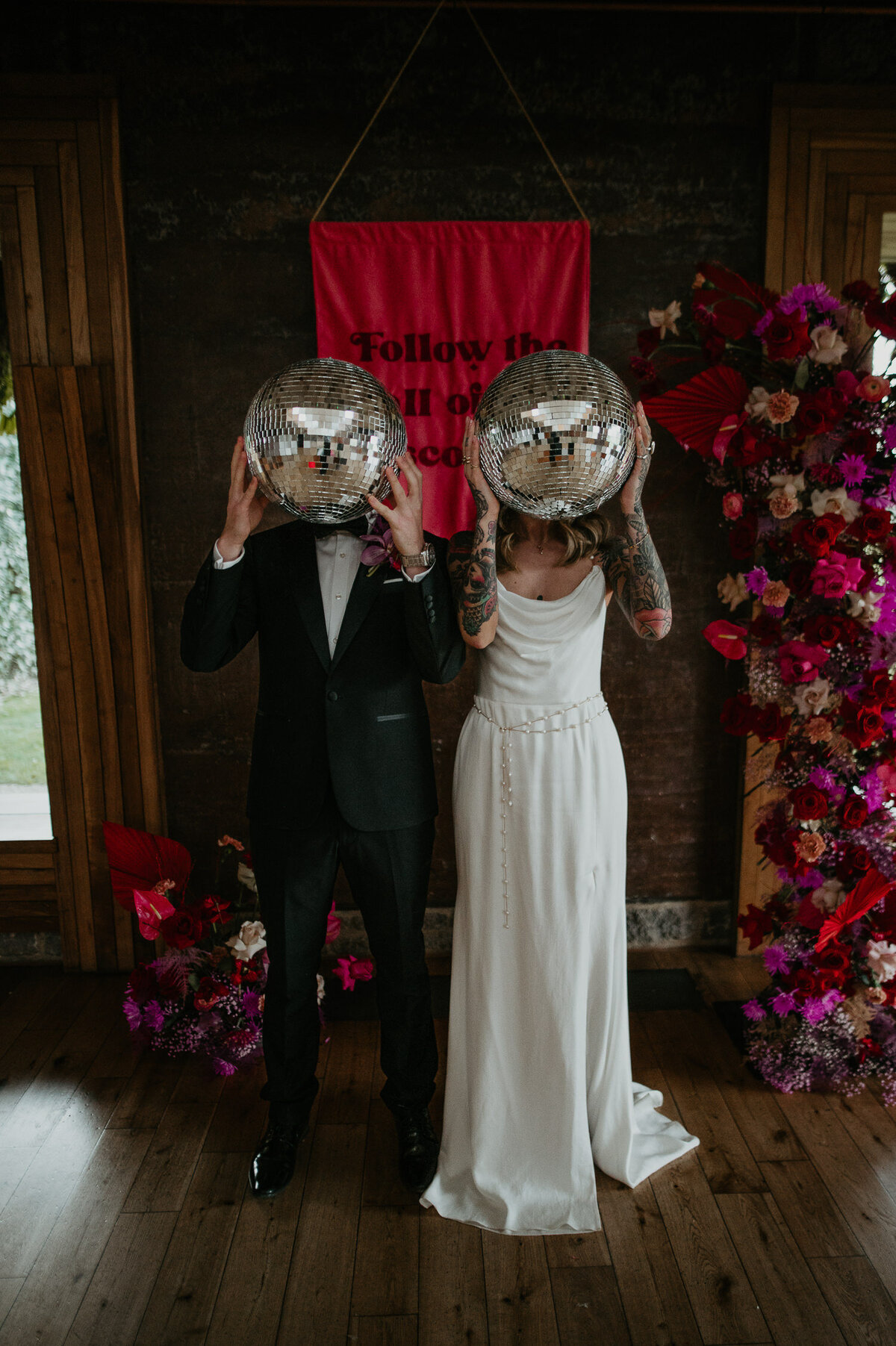 A couple hold disco balls to their faces at a disco themes wedding shoot at Elmore Court.