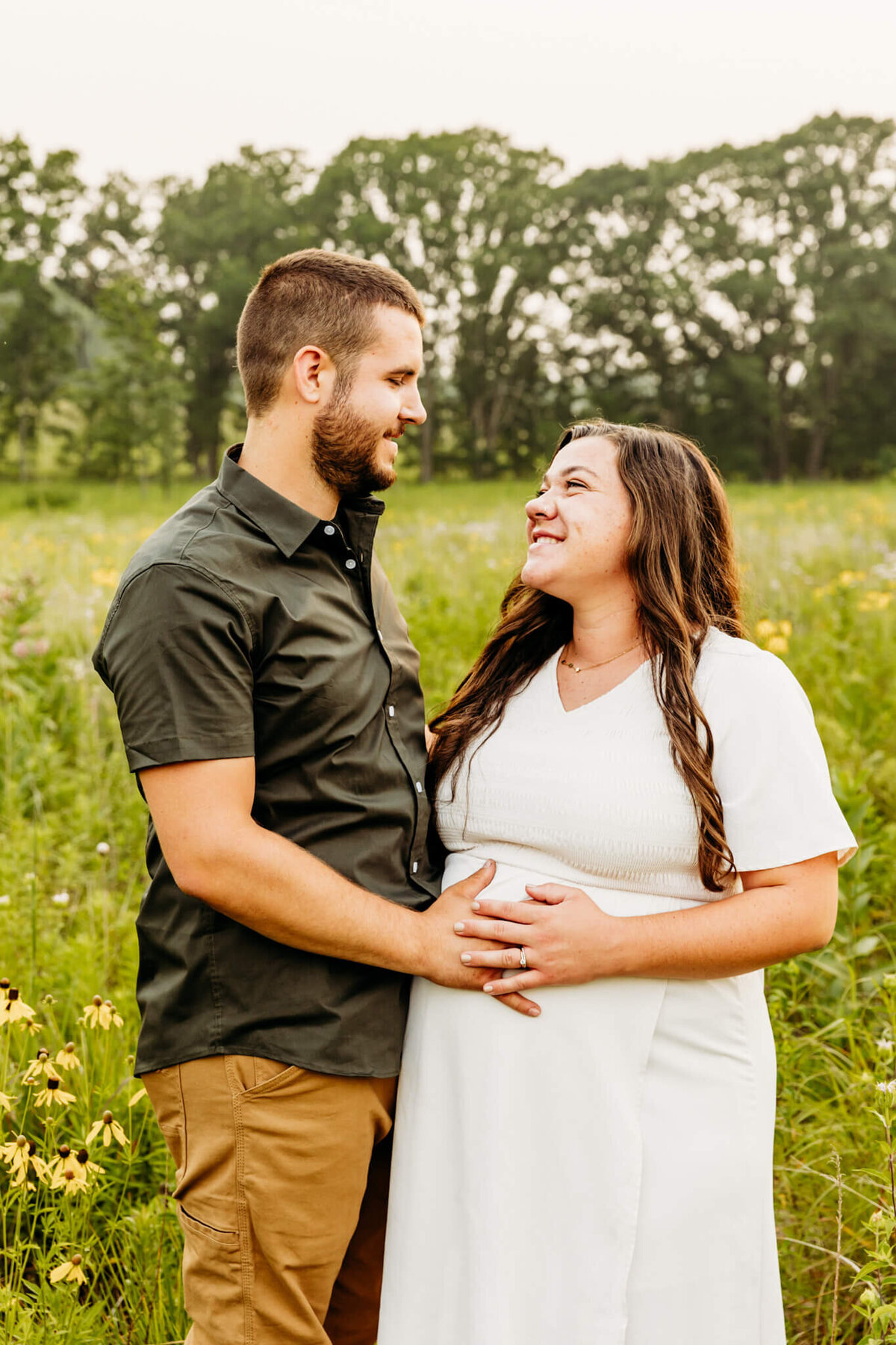 dad and mom holding hands on baby bump and laughing by Ashley Kalbus