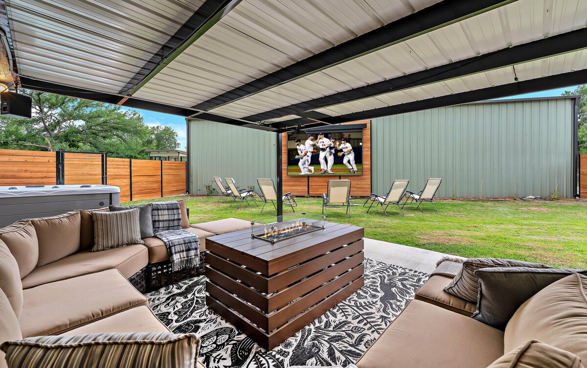 Large outdoor entertainment area with propane fire pit, projector and covered seating area at this three-bedroom, three-bathroom vacation rental home with free wifi, outdoor theater, hot tub, propane grill and private yard in Waco, TX.