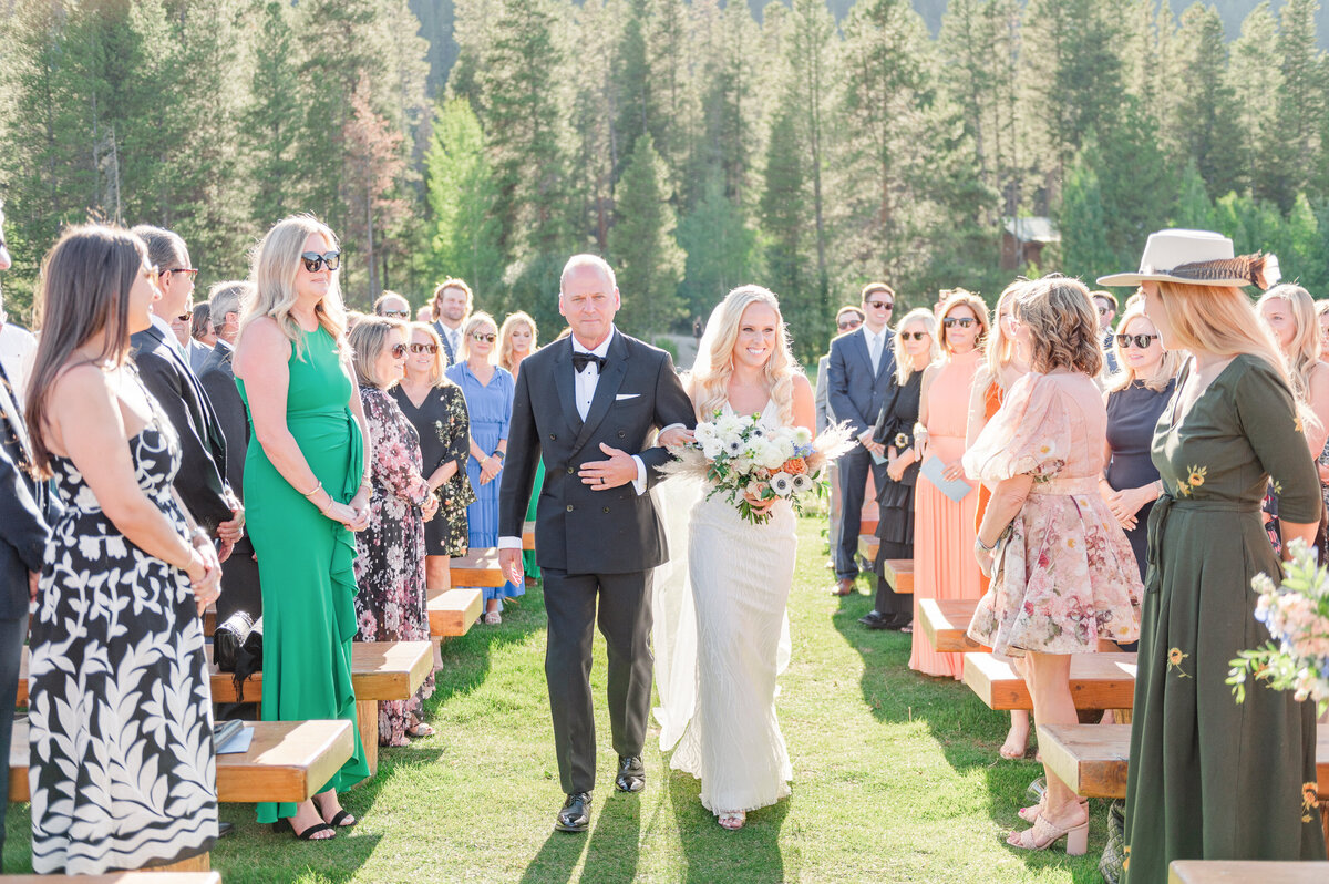 Bride and dad walking down the aisle during an outdoor wedding ceremony at Camp Hale close to Vail, Colorado.