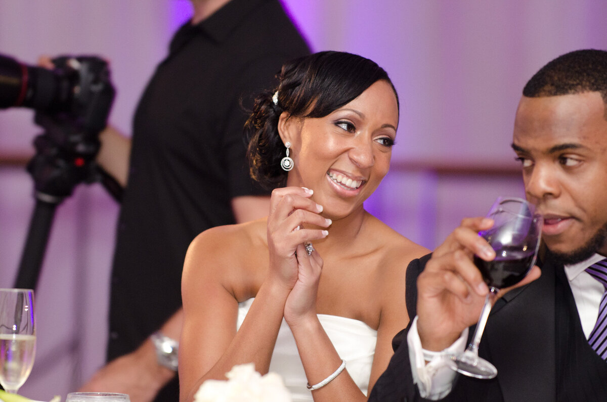 Bride happily looking at her groom while groom drinking wine