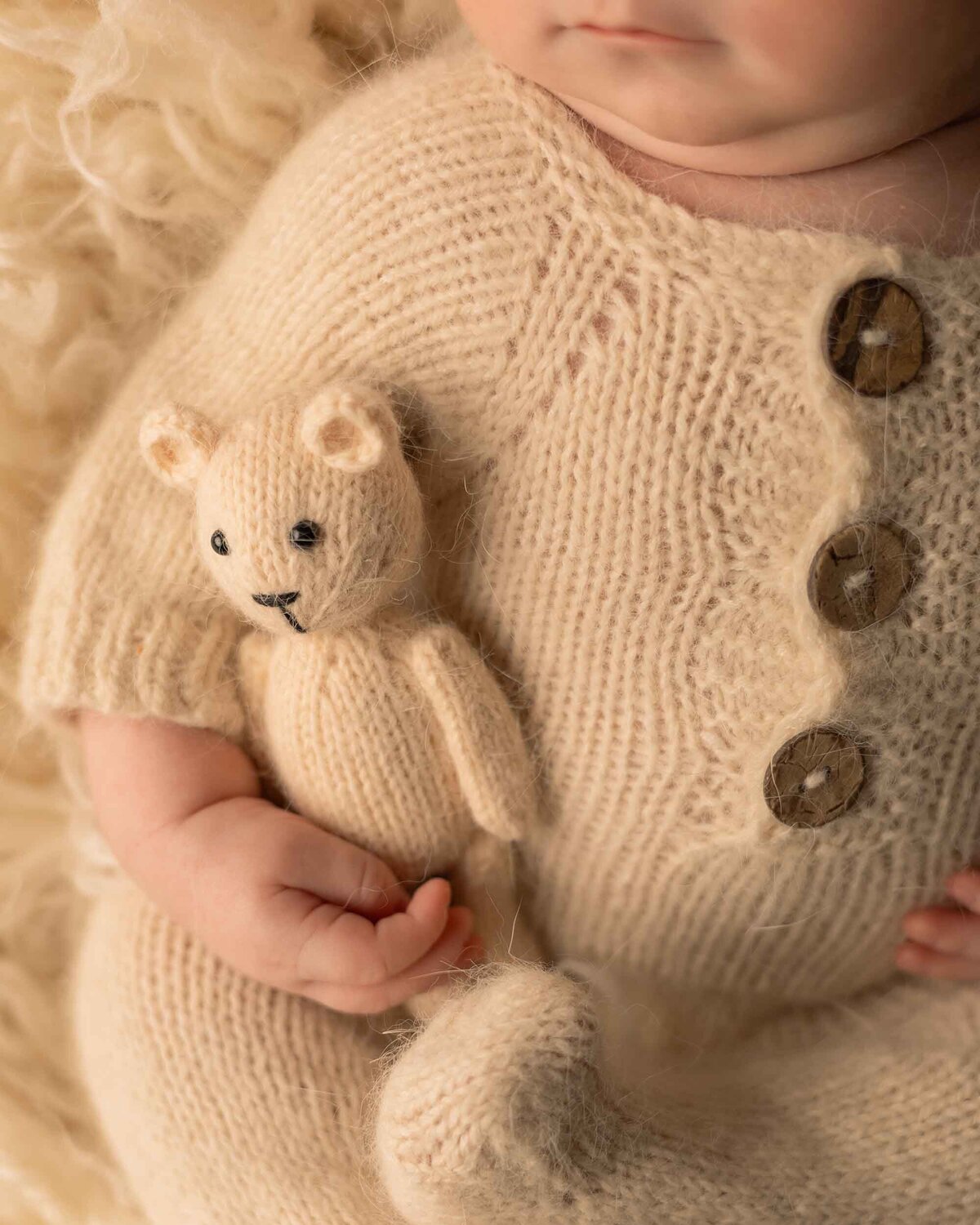 Maddie Rae Photography close up of baby in a neutral outfit on a neutral colored rug. he is holding a little teddy bear, that is the focus