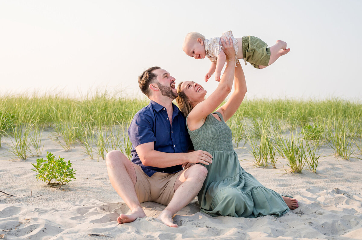 A mother and father holding their baby in the air on the sand in Ocean City, New Jersey