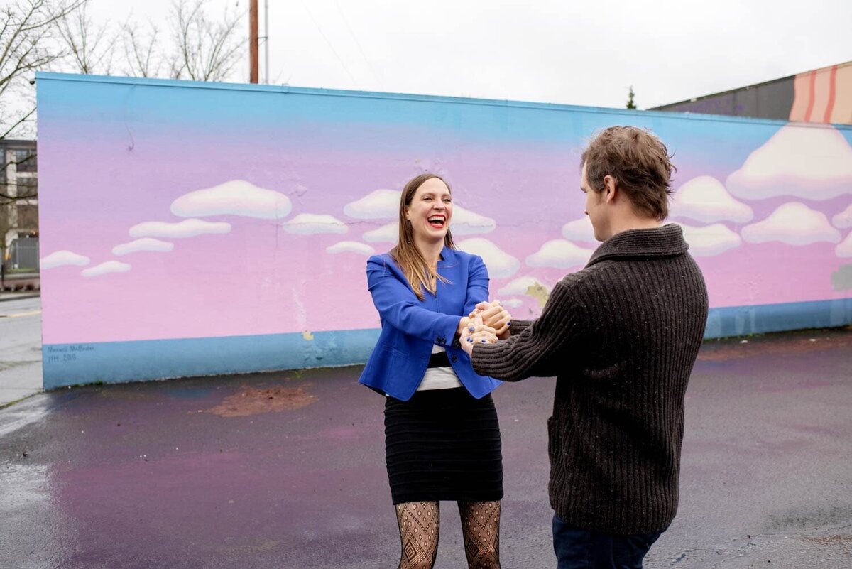 a couple spin and laugh in front of a pink and blue cloud  mural in kenton