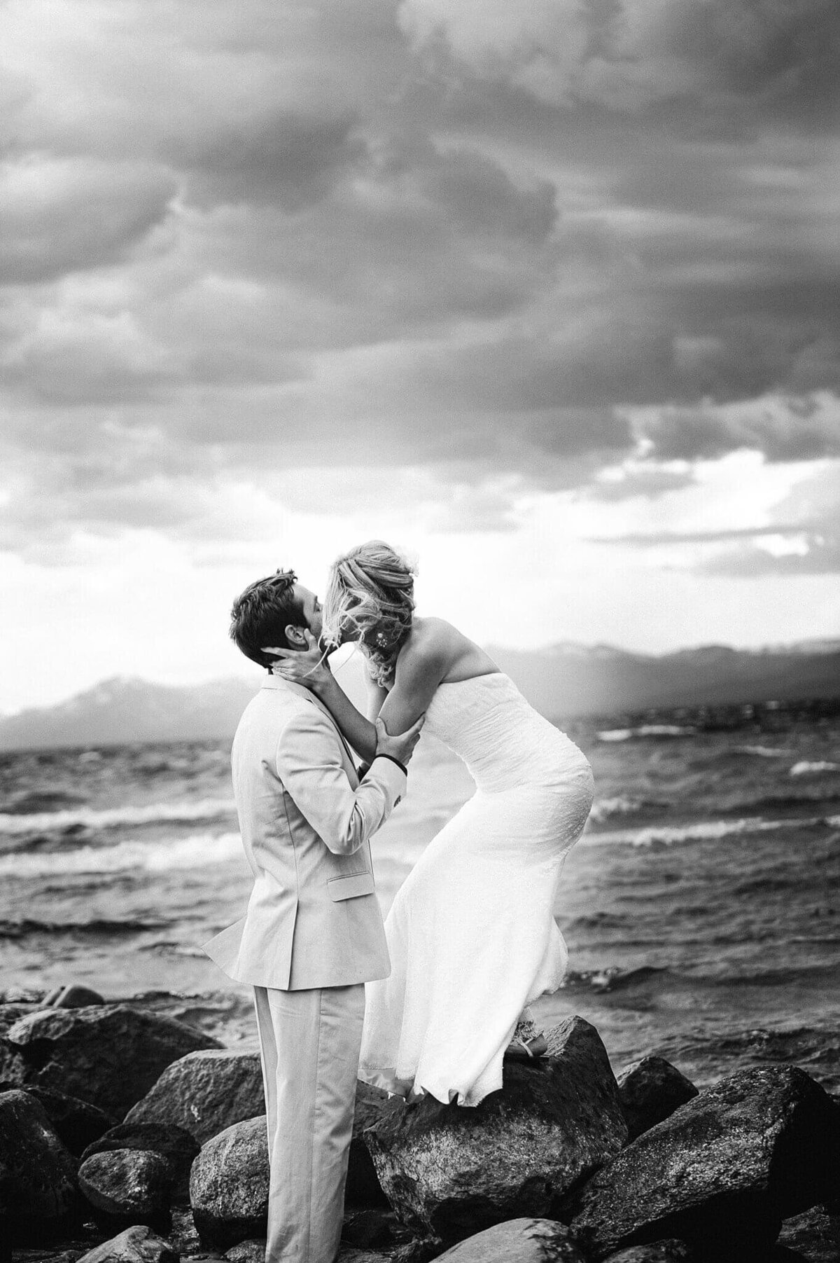 Stormy, windy wedding black and white of couple kissing bride on rocks 