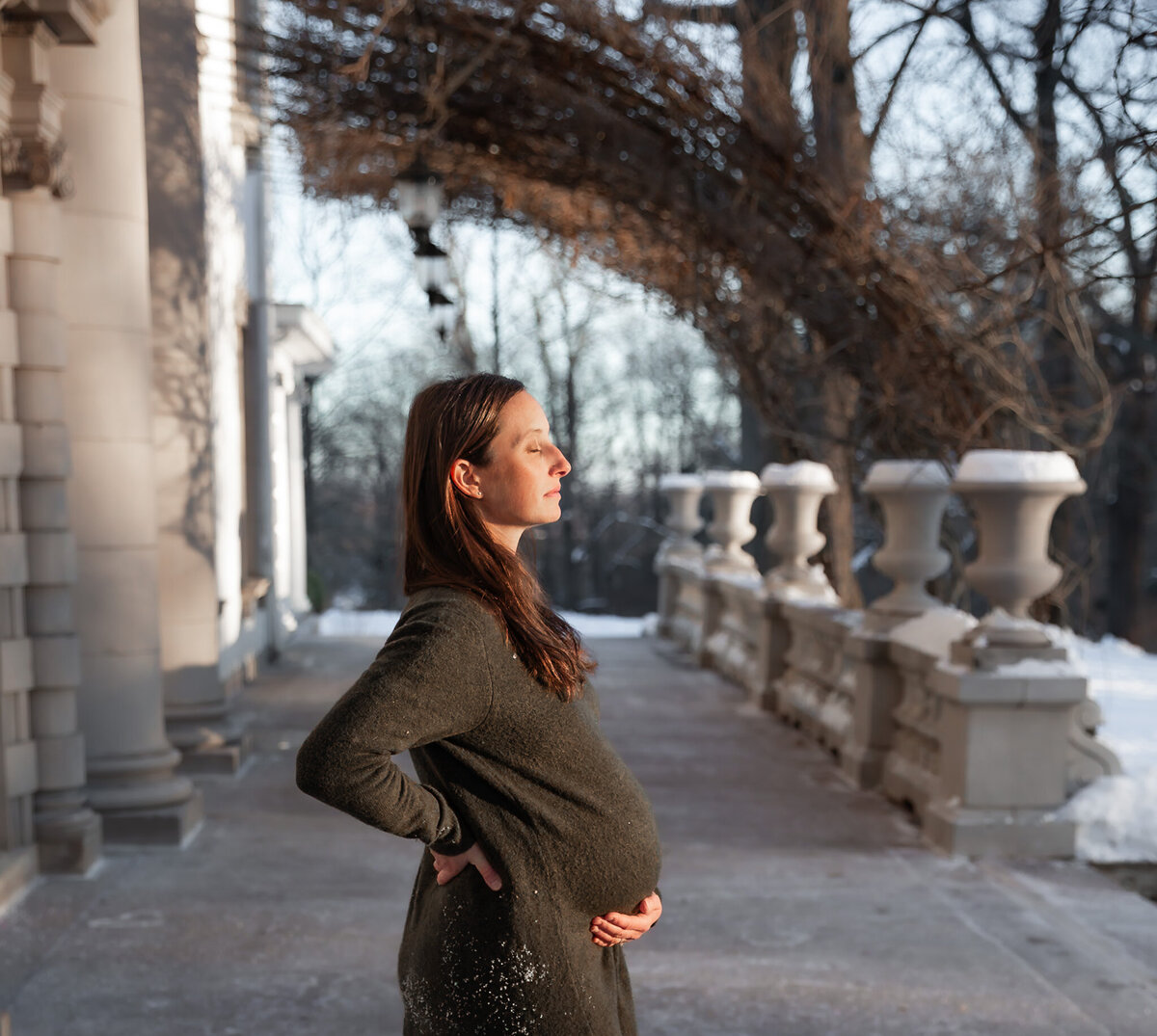 A mother stands on the Liriodendron Mansion porch during maternity photos in Bel Air, Maryland.