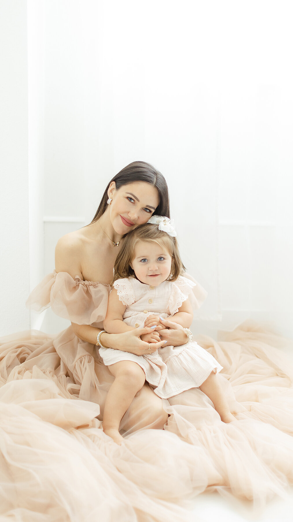 An elegant mommy and me photo taken of a mother and her baby girl sitting on the floor of a Flower Mound photography studio.