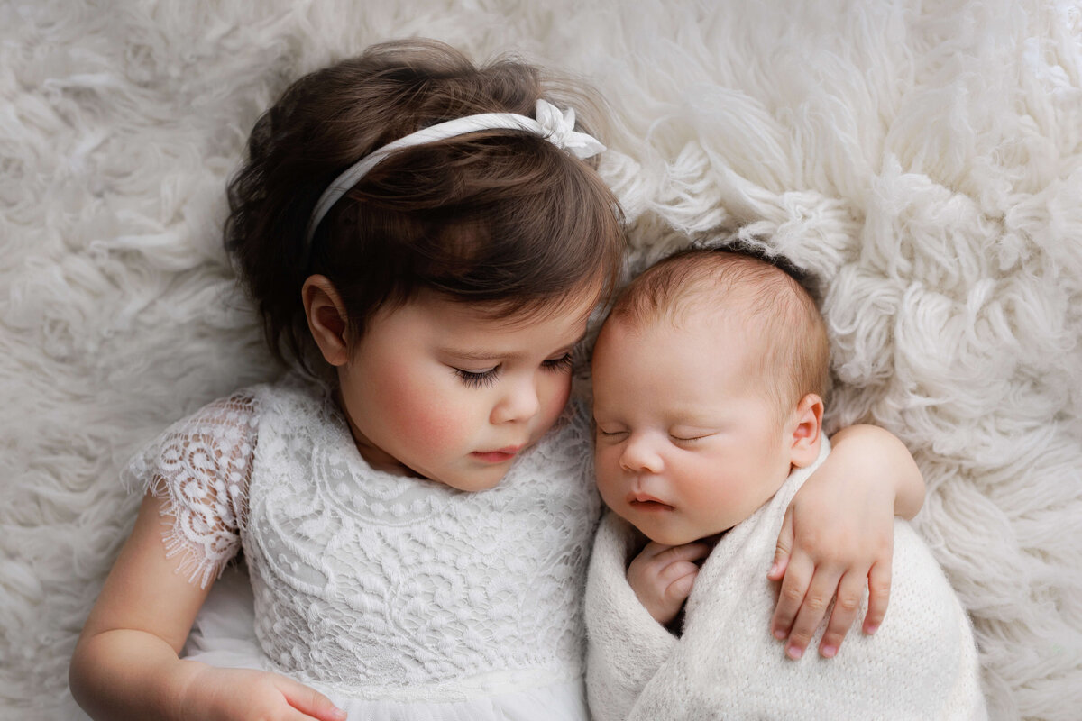 bog sister   holding her little baby brother sleeping  at a photo shoot