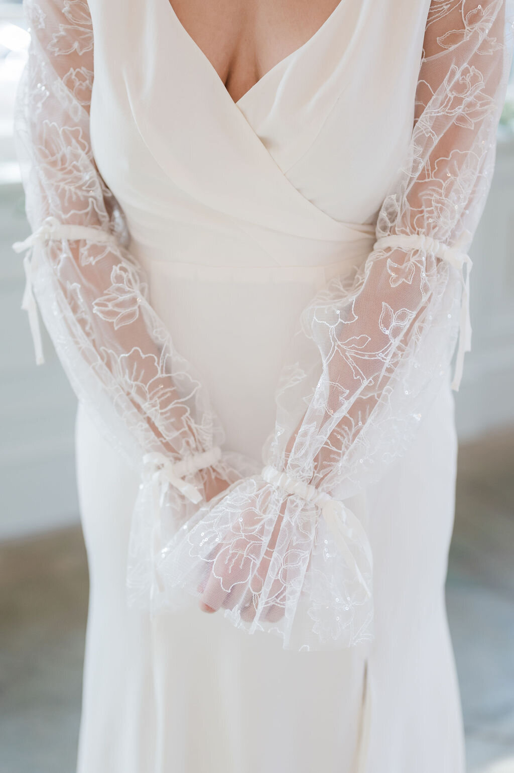 Close-up of the sheer sparkly lace sleeves of the Harlow wedding dress style. The sleeves feature bows at the elbow and wrist.