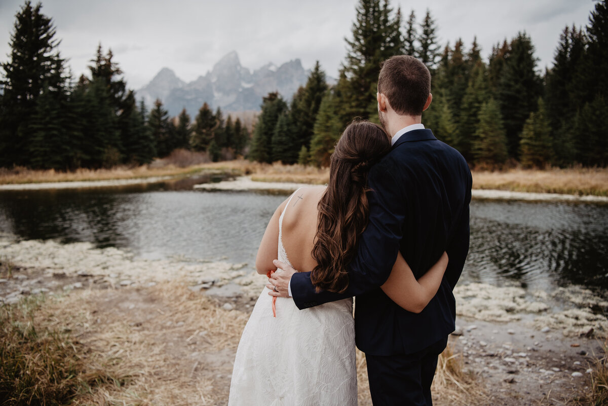 Photographers Jackson Hole capture bride and groom hugging while looking at the Tetons