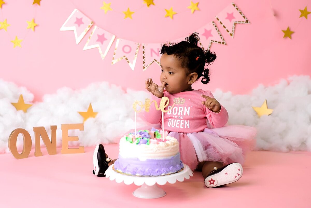 12 month girl in pink with star and cloud theme cake smash backdrop.