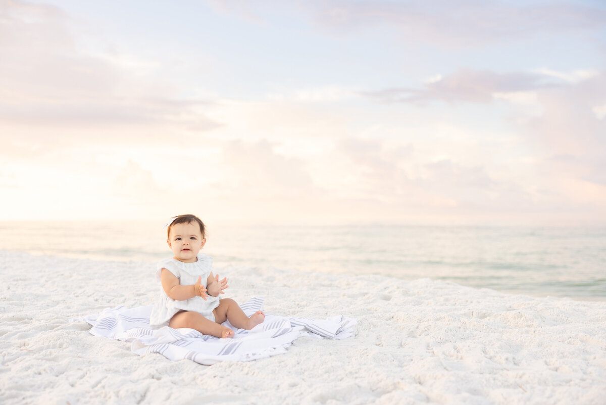 A baby sitting in white sand during sunrise in Watercolor Florida.