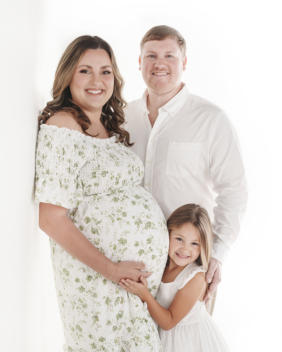 studio maternity portrait of a mom, dad and big sister on a simple white high key backdrop