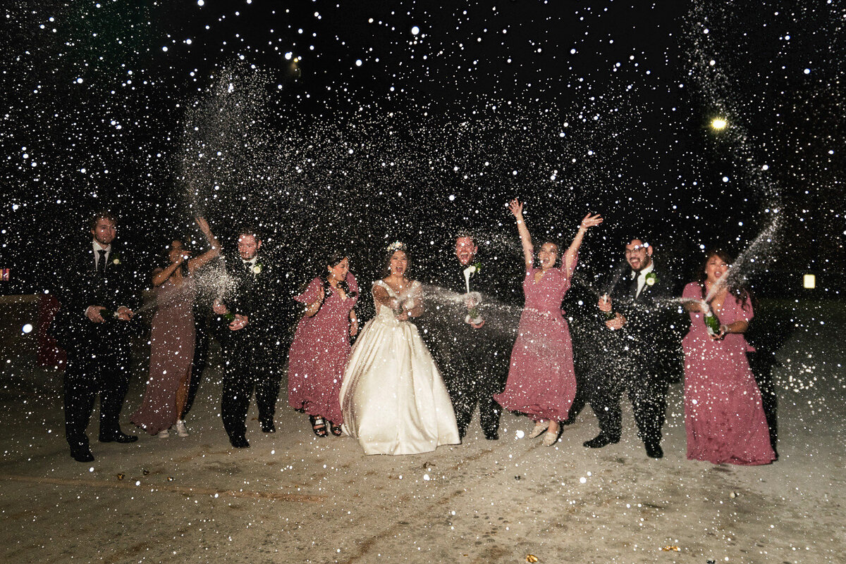 Wedding party sprays multiple bottles of champagne at night.