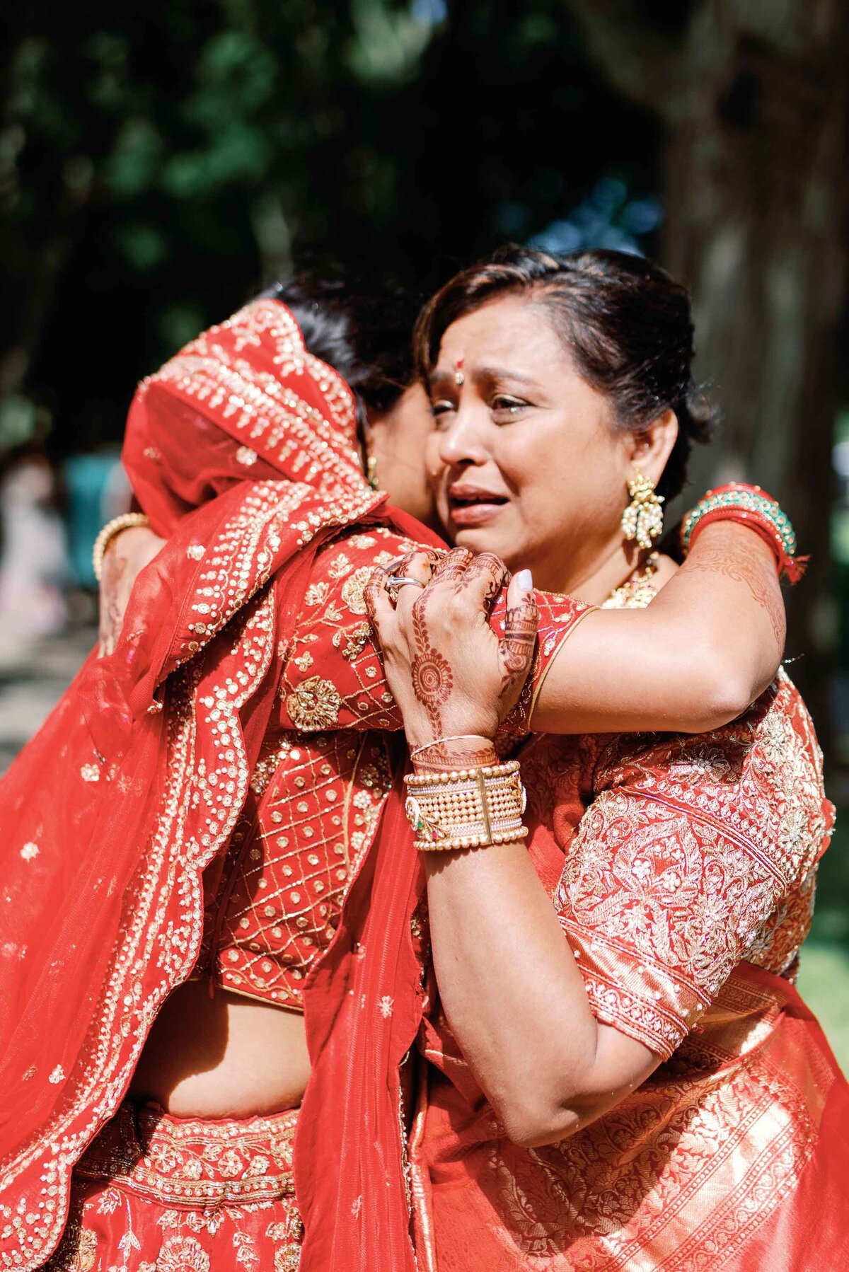 mother hugs bride at indian wedding and red drapery flowing around arms brick house shelburne museum