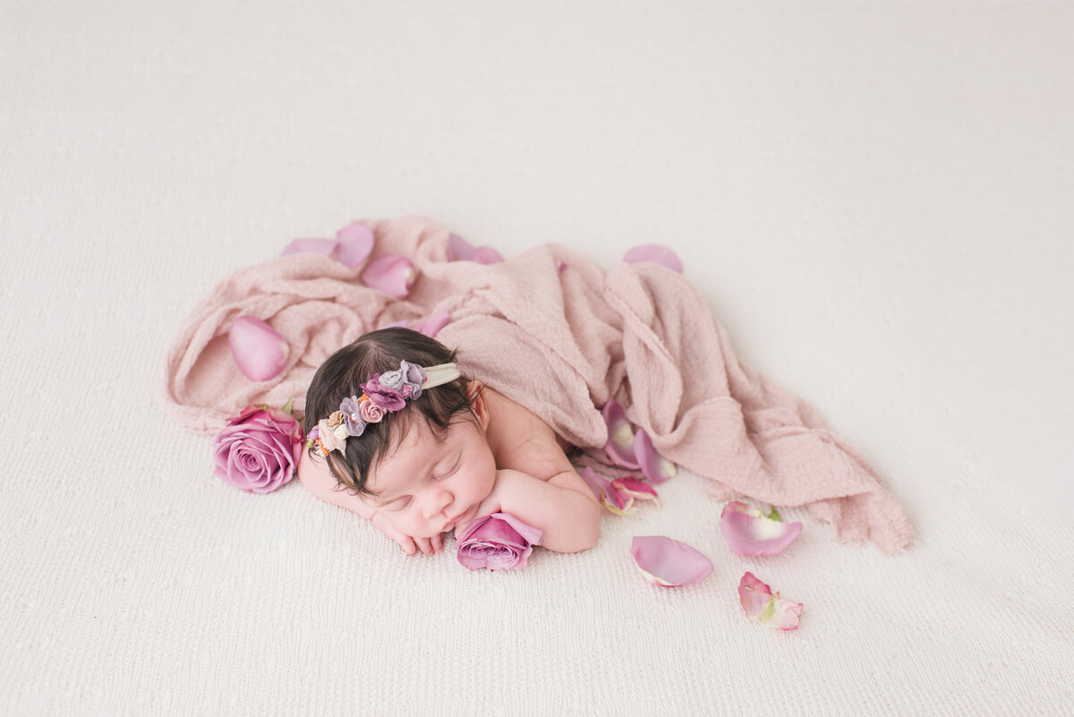 a baby girl with flowers and a pink blanket with white in the back
