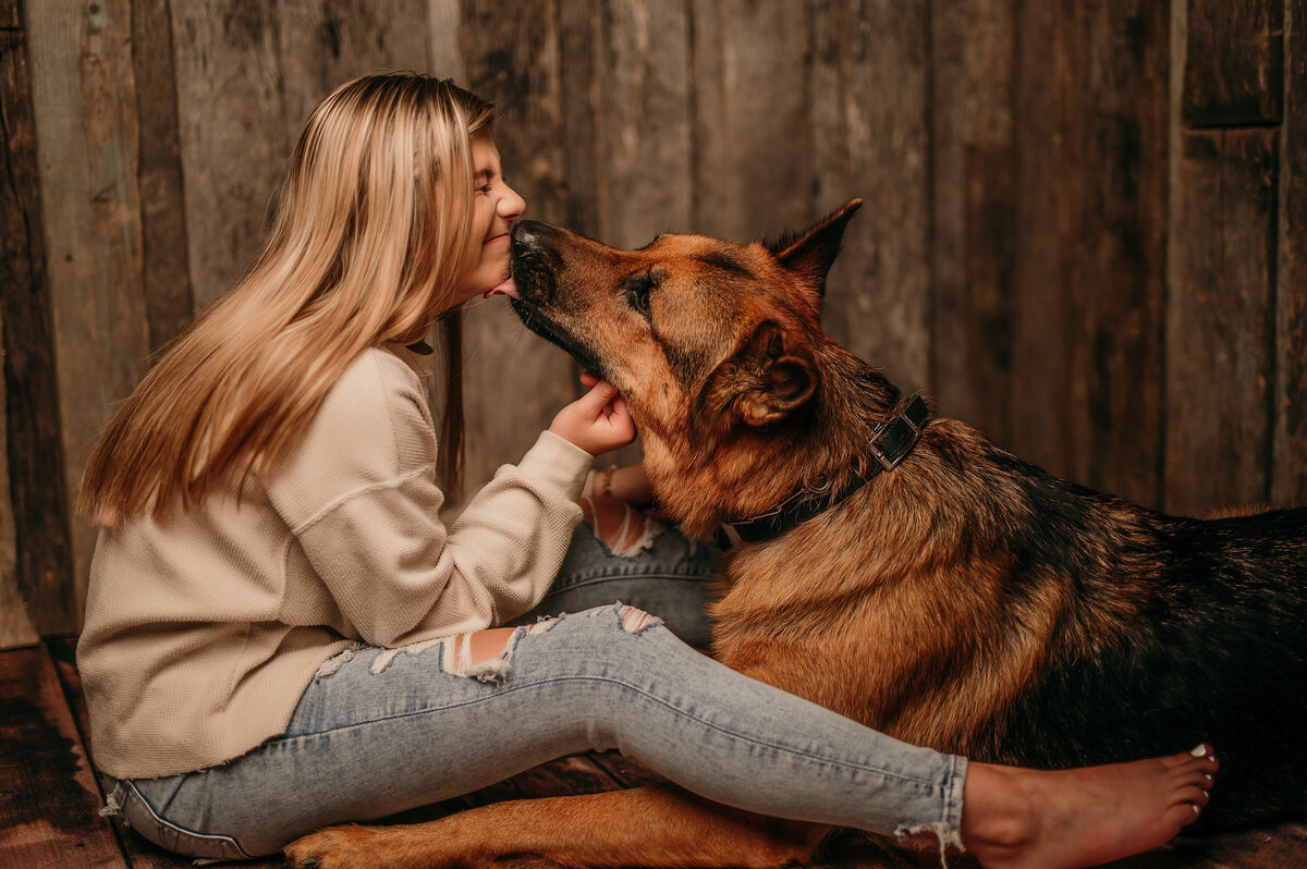 A young woman from Oconomowoc High School sits on the floor of our Waukesha studio getting a kiss from her German Shepherd dog.