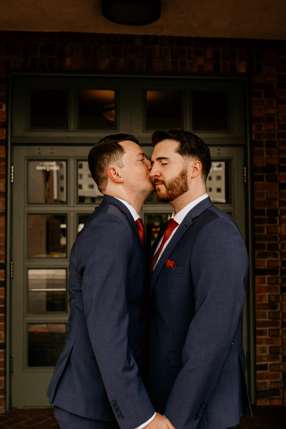 man kissing his grooms cheek in front of a downtown building in Albuquerque