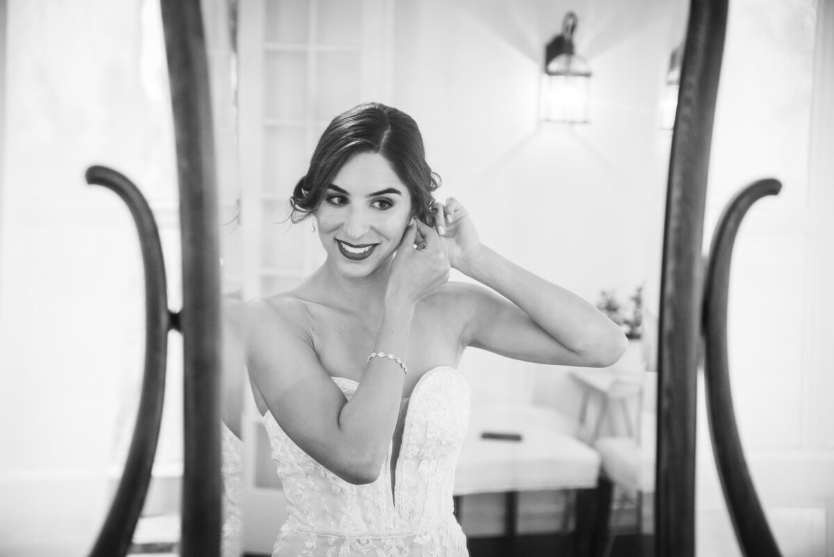 A candid shot of a bride looking into a mirror and putting in her earring.