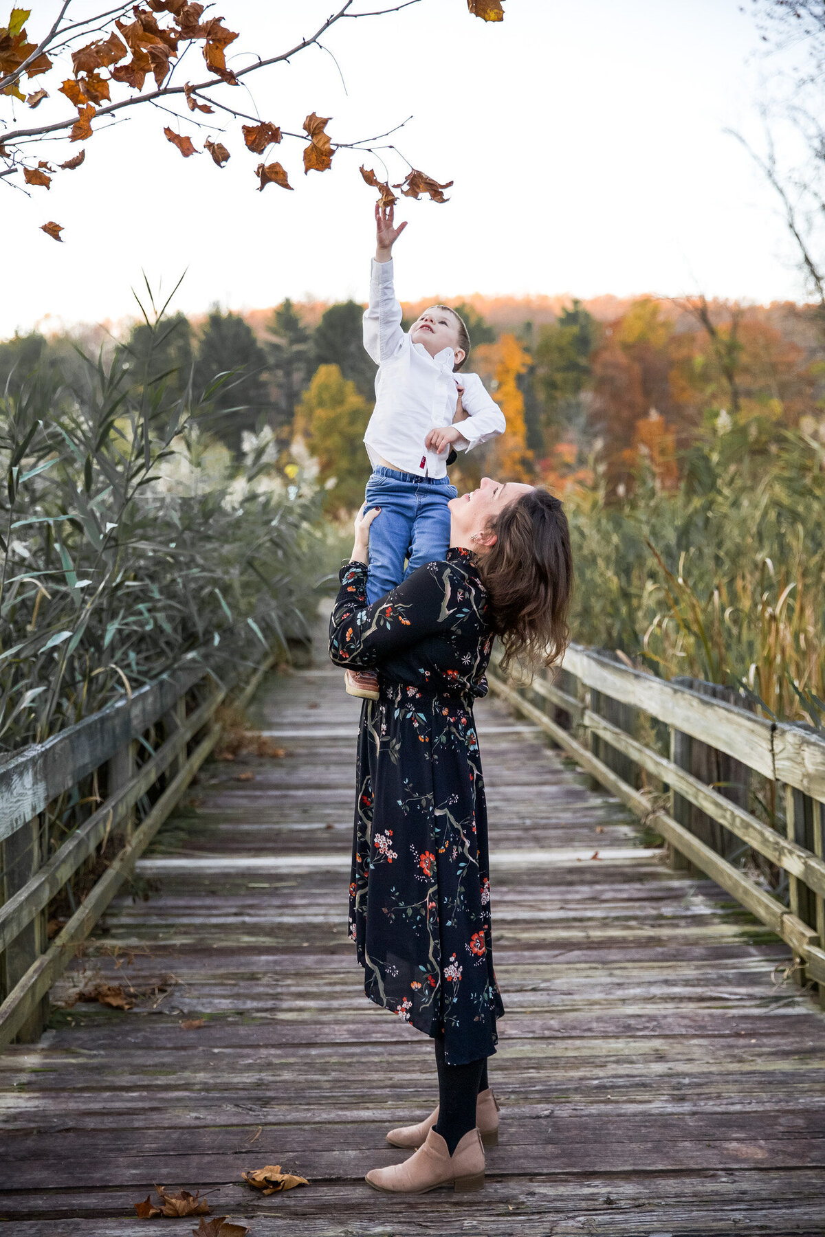 A Bel Air, Maryland mother lifts her son to touch the trees during lifestyle family photos in Bel Air, Maryland at Harford Glen Park.