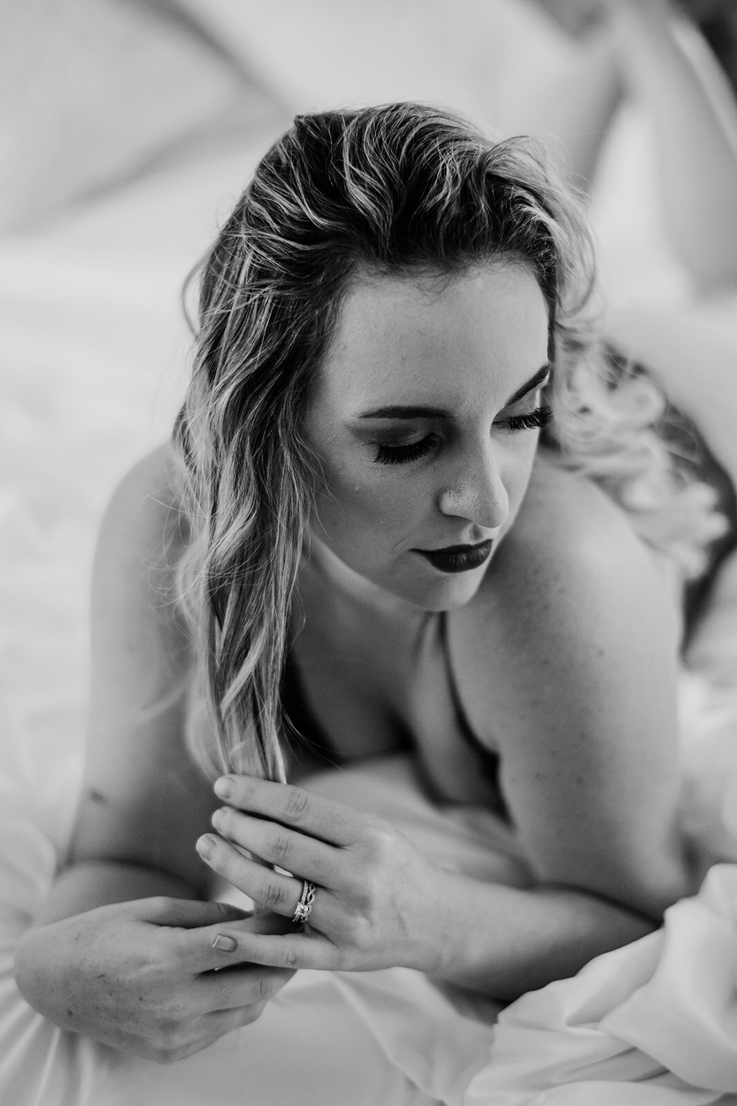 black and white boudoir pictures with woman laying on her stomach on her bed while looking over her shoulder and playing with her hair captured by Baltimore photographers