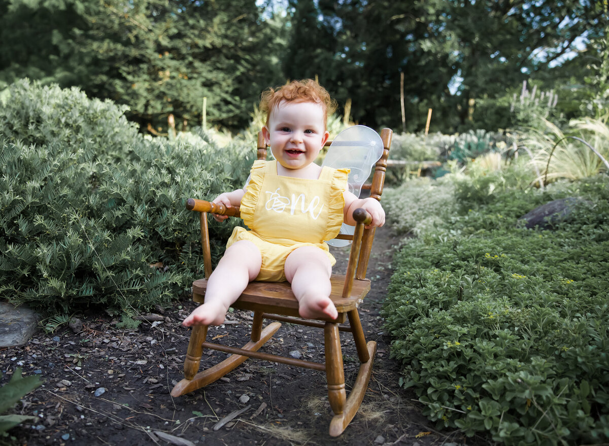 a one year old baby smiles on a rocking chair in Cylburn Arboretum in Baltimore, Maryland during her 1st birthday milestone pictures