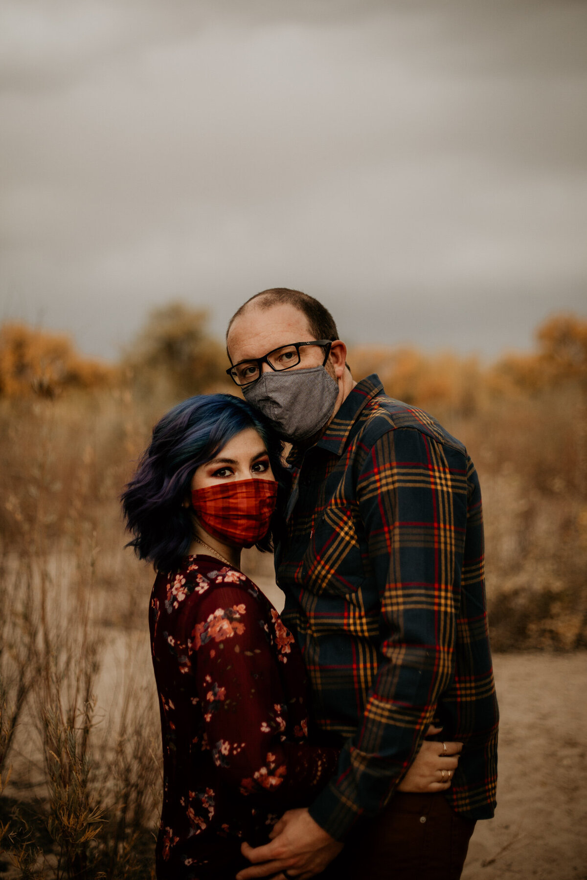 couple standing close wearing masks on the beach