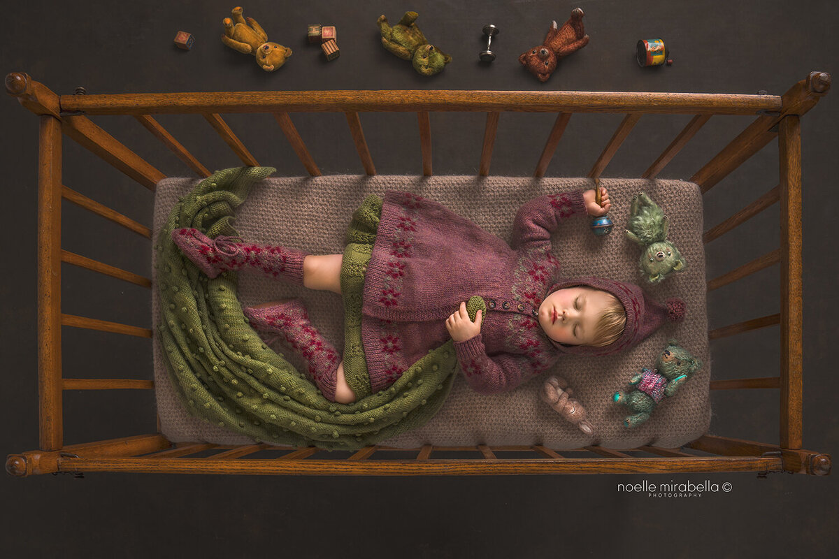 Toddler sleeping in vintage wooden crib with vintage toys on the floor.