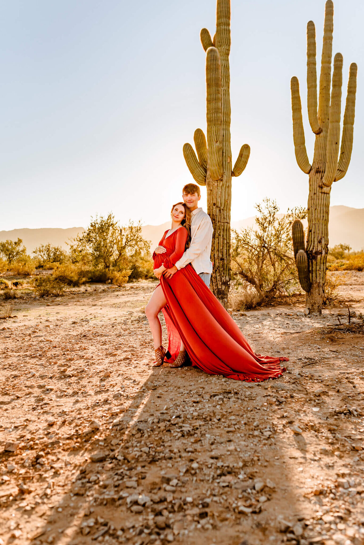 young couple with rust dress, holding their baby belly for their maternity photography session in Arizona