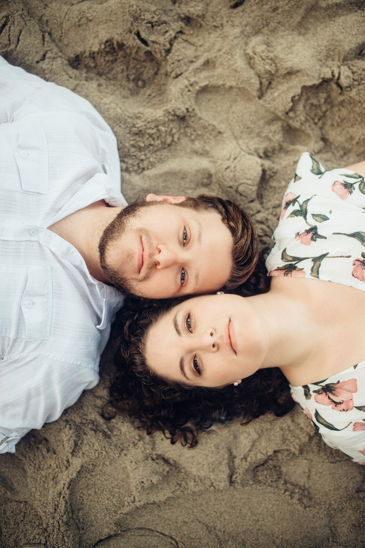 Engagement Photograph Of  Man And Woman  Laying On a Dark Sand Los Angeles