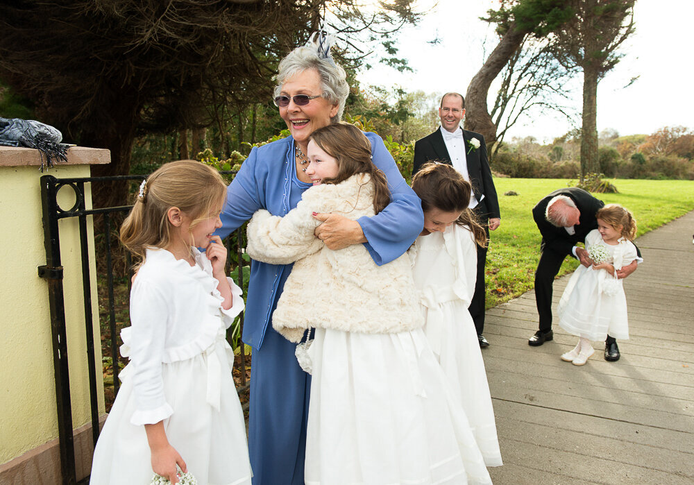 Grandmother wearing blue hugging her flower girl grandchildren at the gate of a church in Kenmare