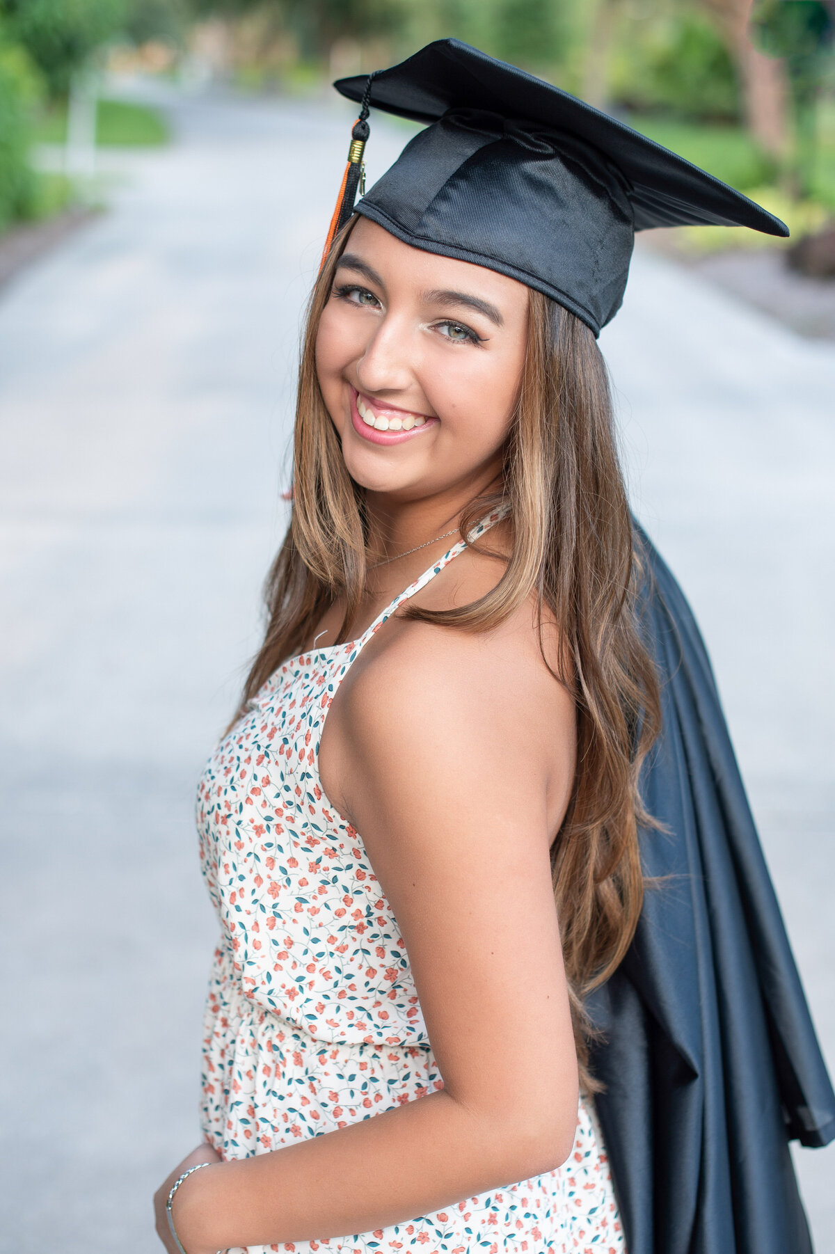 High school senior girl wearing cap holds gown over shoulder.