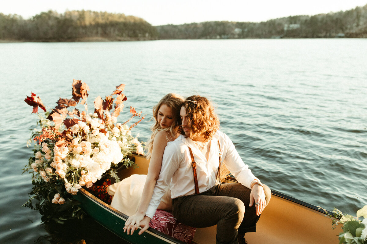Boho bride and groom sitting in a canoe decorated with flowers on a lake